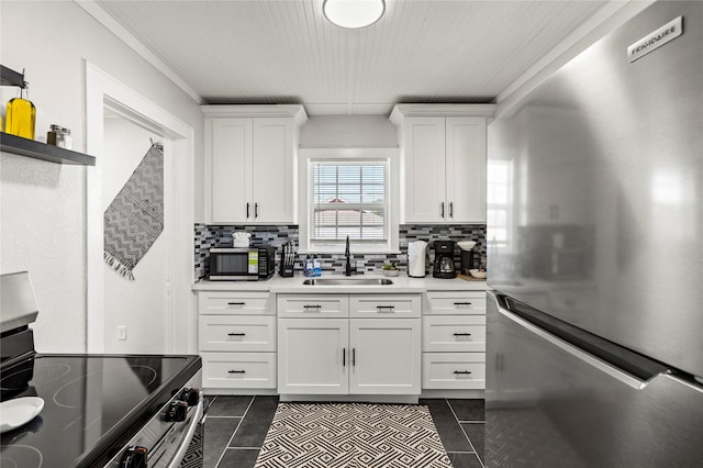 kitchen featuring white cabinetry, dark tile patterned flooring, tasteful backsplash, a sink, and appliances with stainless steel finishes