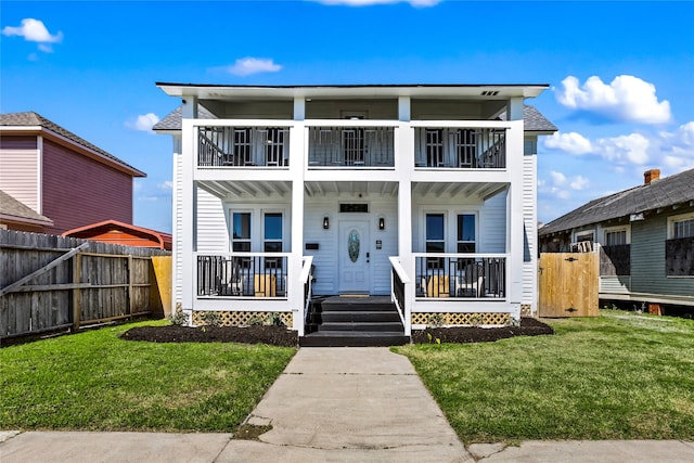 view of front of house featuring a porch, fence, a balcony, and a front lawn