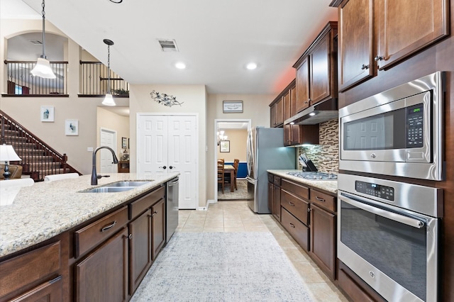 kitchen with decorative light fixtures, tasteful backsplash, light stone countertops, a sink, and stainless steel appliances