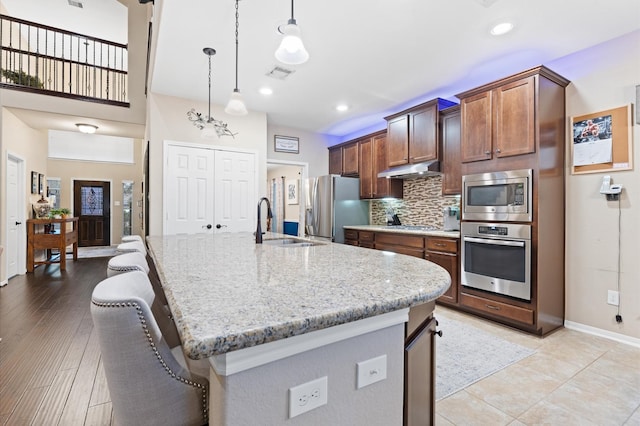 kitchen featuring visible vents, decorative backsplash, light stone countertops, a sink, and stainless steel appliances