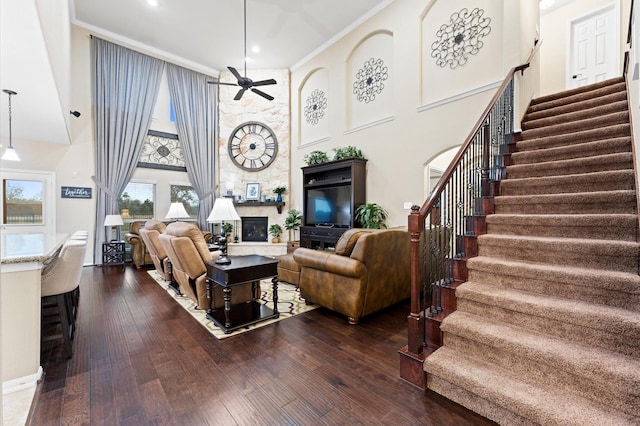 living area with a ceiling fan, a towering ceiling, a fireplace, dark wood finished floors, and stairs