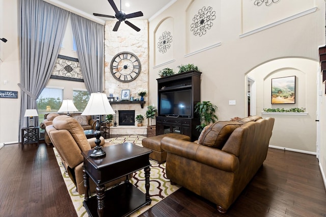 living room featuring a high ceiling, ceiling fan, a stone fireplace, baseboards, and ornamental molding