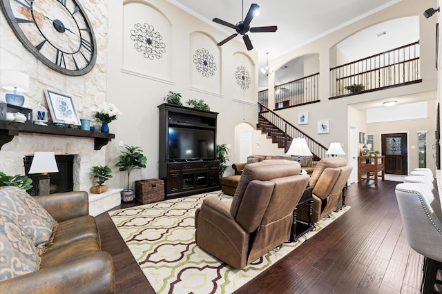living area with a fireplace, wood-type flooring, stairs, a ceiling fan, and a towering ceiling
