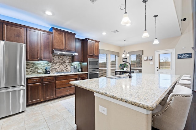kitchen featuring decorative backsplash, appliances with stainless steel finishes, a sink, light stone counters, and under cabinet range hood