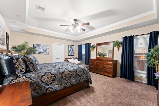 carpeted bedroom featuring a ceiling fan, a tray ceiling, visible vents, and ornamental molding