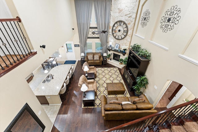 living area featuring a high ceiling, arched walkways, a large fireplace, stairs, and wood finished floors
