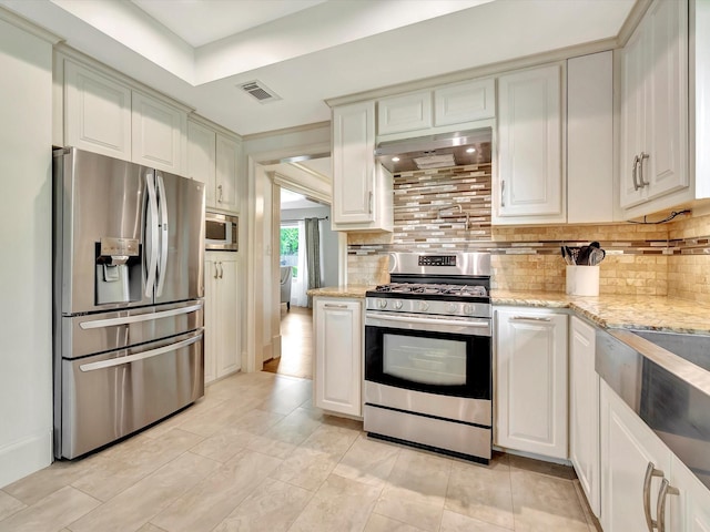 kitchen with stainless steel appliances, backsplash, exhaust hood, light stone countertops, and white cabinets