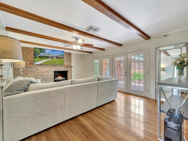 living room with beam ceiling, a ceiling fan, a stone fireplace, and light wood-type flooring