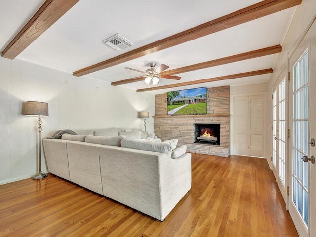 living room featuring beamed ceiling, light wood-style floors, a fireplace, and a ceiling fan