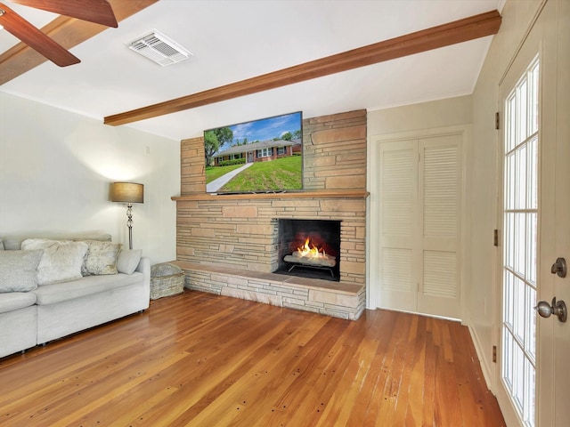 living room with a stone fireplace, beam ceiling, and wood-type flooring
