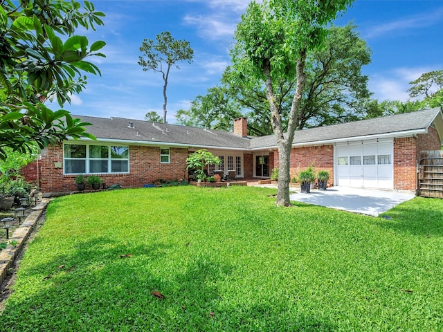 rear view of house with a garage, a chimney, a yard, and brick siding