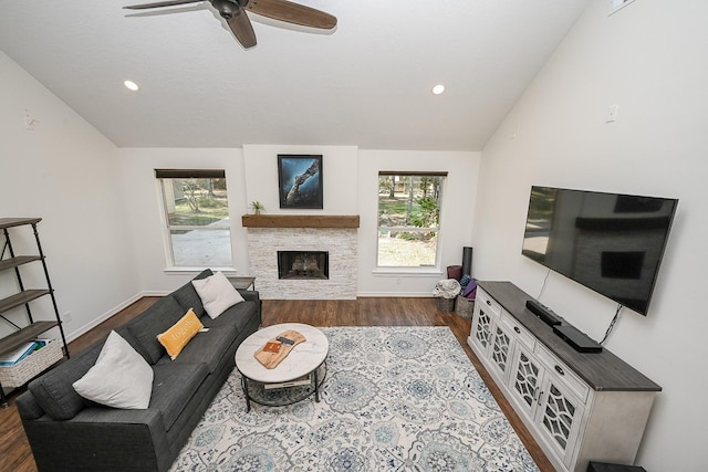 living room featuring ceiling fan, a stone fireplace, baseboards, wood finished floors, and lofted ceiling
