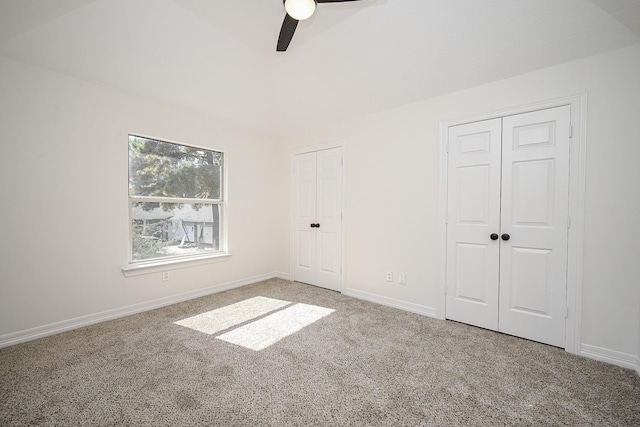 unfurnished bedroom featuring a ceiling fan, vaulted ceiling, baseboards, multiple closets, and carpet flooring