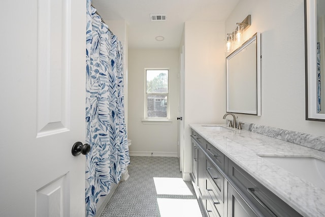bathroom with a sink, double vanity, tile patterned floors, baseboards, and visible vents