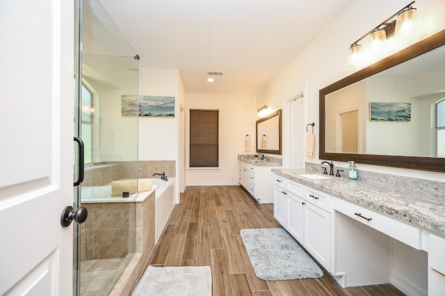 full bath featuring visible vents, wood finished floors, a bath, two vanities, and a sink