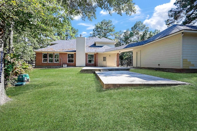rear view of house featuring brick siding, a patio area, a yard, and a chimney