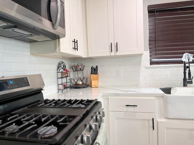 kitchen featuring decorative backsplash, light stone countertops, a sink, white cabinets, and stainless steel appliances