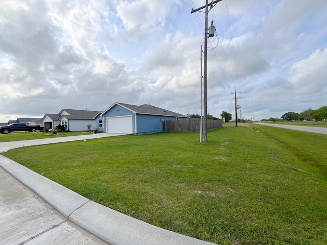 view of yard featuring an attached garage, fence, and concrete driveway