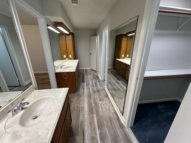 full bathroom featuring wood finished floors, a sink, two vanities, and visible vents