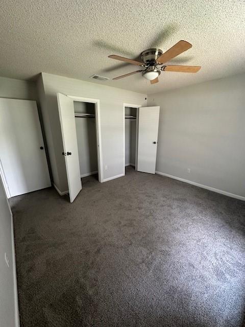 unfurnished bedroom featuring multiple closets, baseboards, dark colored carpet, and a textured ceiling