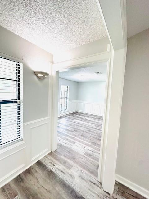 hall with a textured ceiling, wainscoting, wood finished floors, and a decorative wall