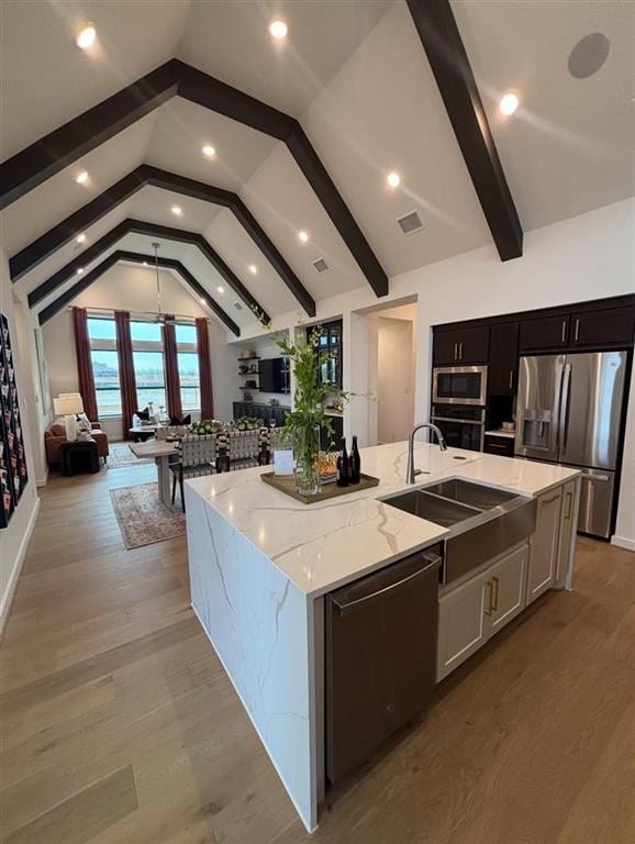 kitchen featuring appliances with stainless steel finishes, a large island with sink, a sink, lofted ceiling with beams, and open floor plan