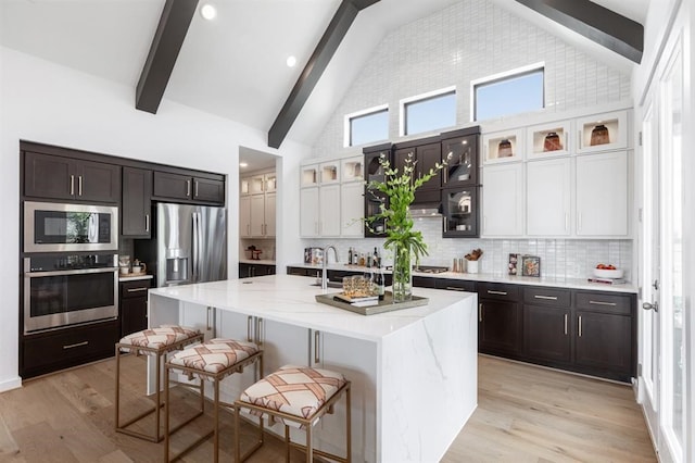 17703 Monarch Vista Ln, Conroe, TX 77302 - kitchen with stainless steel appliances, beamed ceiling, a kitchen breakfast bar, tasteful backsplash, and light wood-style floors