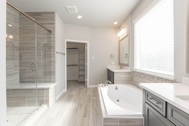 bathroom featuring a walk in closet, two vanities, a bath, a sink, and a stall shower