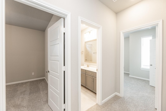 hall with baseboards, a sink, and light carpet