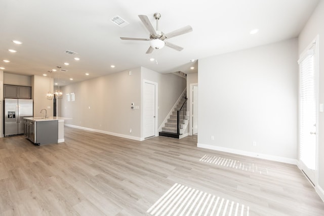 unfurnished living room with recessed lighting, stairway, baseboards, and ceiling fan with notable chandelier