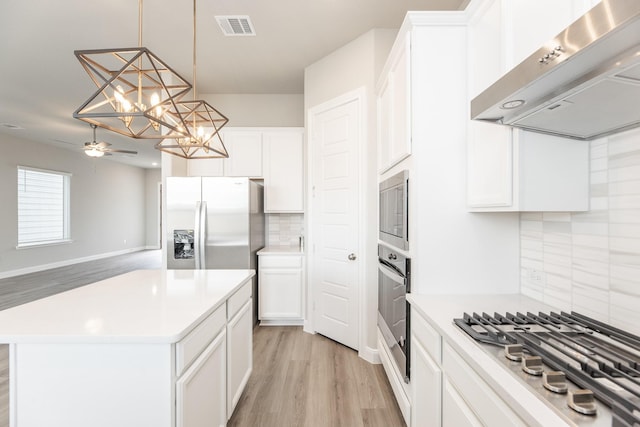 3011 Valley Peak Dr, Houston, TX 77063 - kitchen with exhaust hood, appliances with stainless steel finishes, light wood finished floors, ceiling fan with notable chandelier, and backsplash