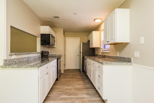 kitchen with visible vents, white cabinets, a sink, light wood-style flooring, and stainless steel appliances