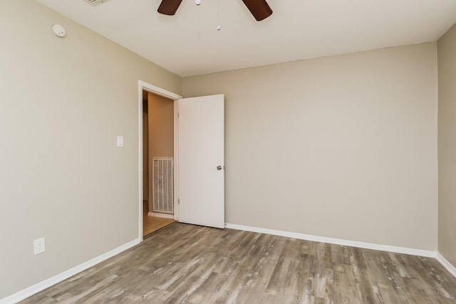 empty room with baseboards, a ceiling fan, wood finished floors, and visible vents