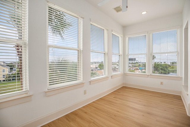 unfurnished sunroom featuring baseboards, plenty of natural light, wood finished floors, and visible vents