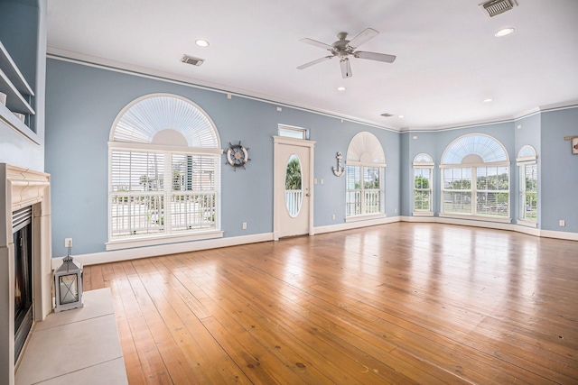 unfurnished living room featuring crown molding, a fireplace with raised hearth, ceiling fan, and visible vents