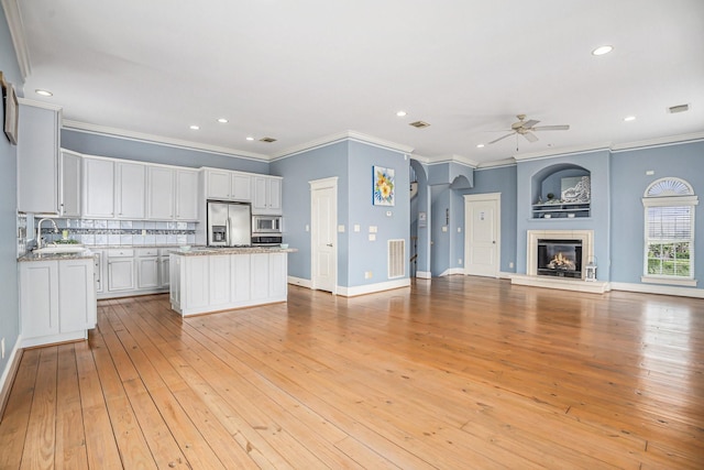 kitchen with open floor plan, ceiling fan, a center island, appliances with stainless steel finishes, and backsplash