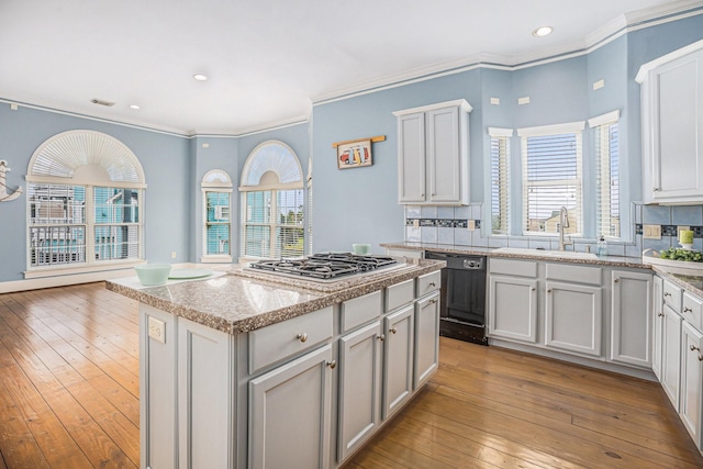kitchen featuring stainless steel gas stovetop, decorative backsplash, black dishwasher, and a sink