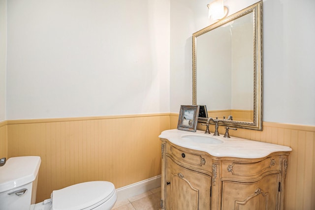 half bathroom with vanity, toilet, tile patterned flooring, and a wainscoted wall