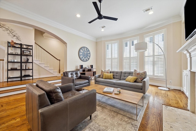 living room with crown molding, arched walkways, a ceiling fan, visible vents, and stairway