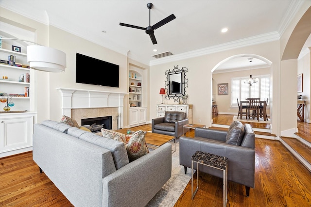 living room featuring ornamental molding, built in features, wood finished floors, arched walkways, and ceiling fan with notable chandelier