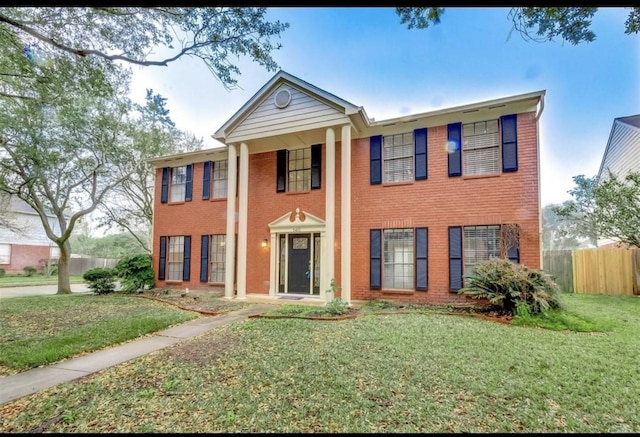 neoclassical / greek revival house with brick siding, a front lawn, and fence