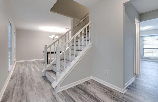 stairway featuring baseboards, an inviting chandelier, and wood finished floors