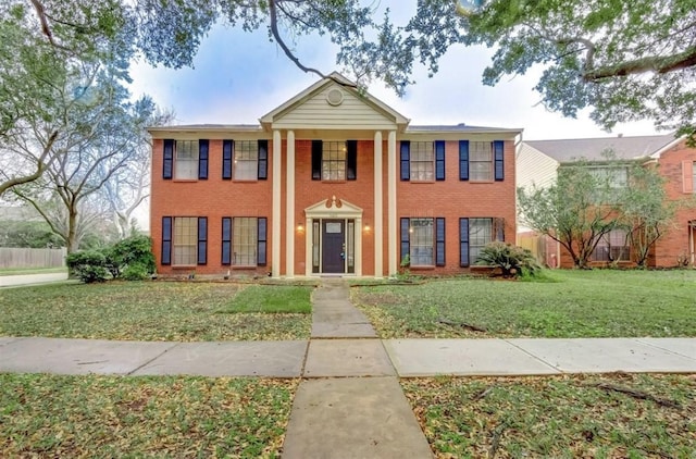 greek revival inspired property featuring brick siding, fence, and a front yard