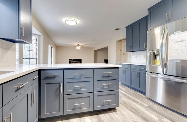 kitchen featuring decorative backsplash, a ceiling fan, light countertops, a peninsula, and stainless steel fridge