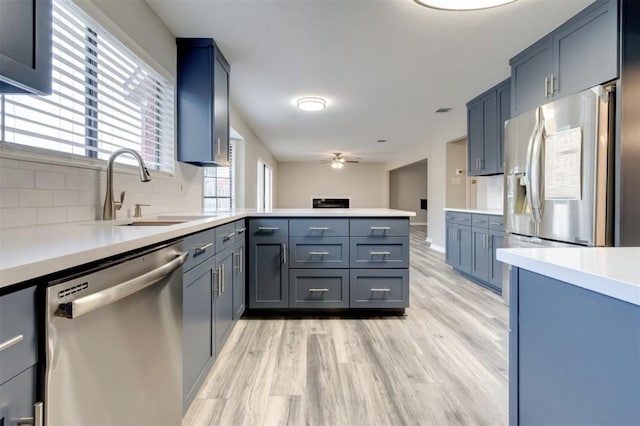 kitchen with a peninsula, appliances with stainless steel finishes, a sink, and light wood-style flooring