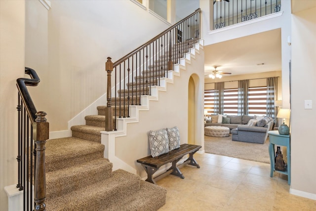 staircase with baseboards, ceiling fan, a high ceiling, arched walkways, and carpet flooring