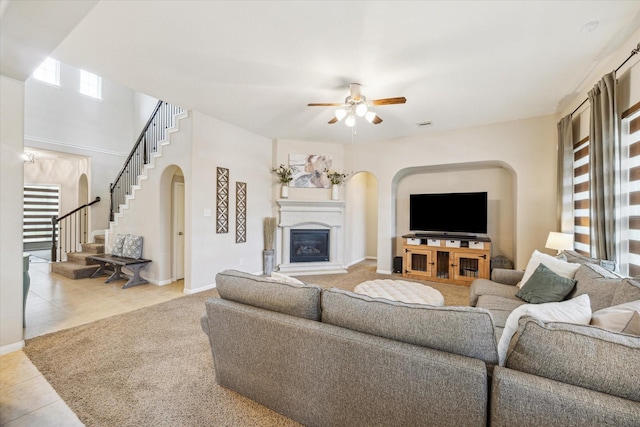tiled living room featuring a ceiling fan, stairs, a glass covered fireplace, baseboards, and arched walkways