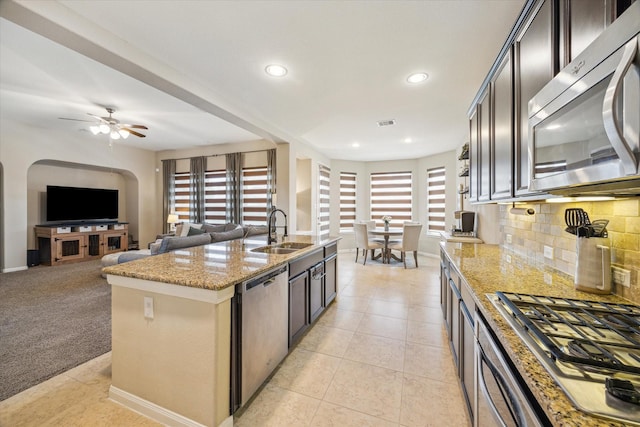 kitchen featuring a kitchen island with sink, light tile patterned flooring, light stone countertops, a sink, and stainless steel appliances