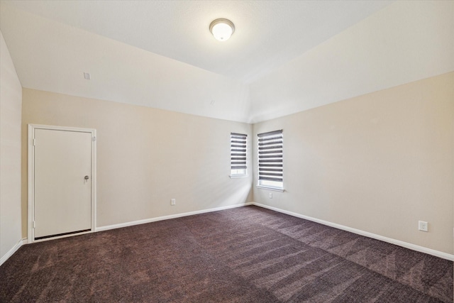 unfurnished room featuring baseboards, lofted ceiling, and dark colored carpet