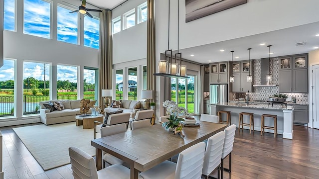 dining area featuring ceiling fan, visible vents, dark wood-type flooring, and a towering ceiling